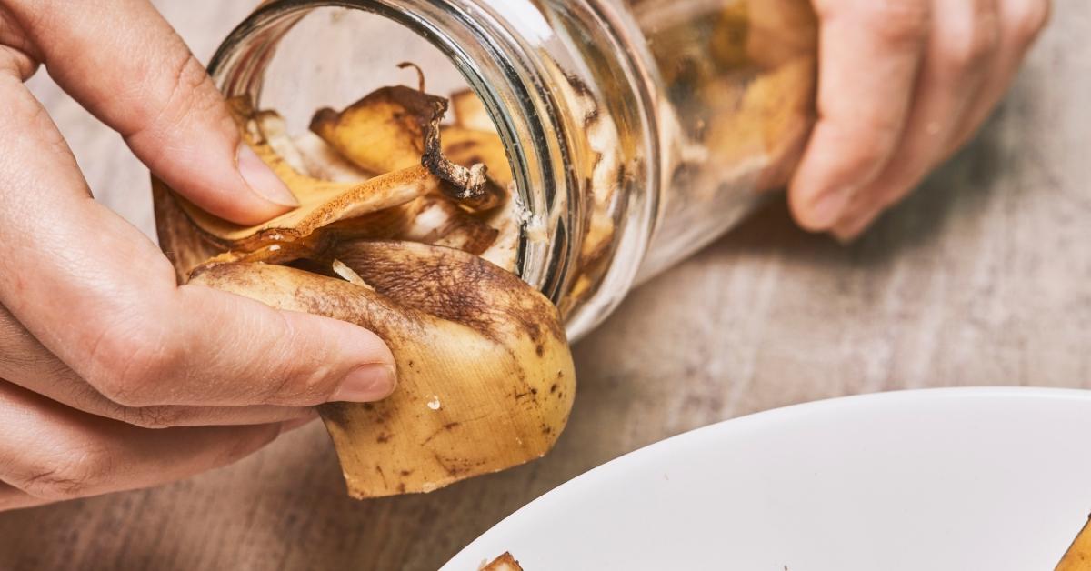 A hand pulls an old banana peel out of a jar. 