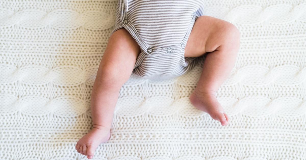 Unrecognizable baby boy wearing organic onesie lying on bed, close up of his legs