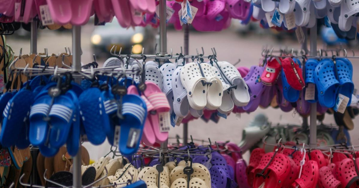 Several sizes and colors of Crocs shoes hang on a wall in a store