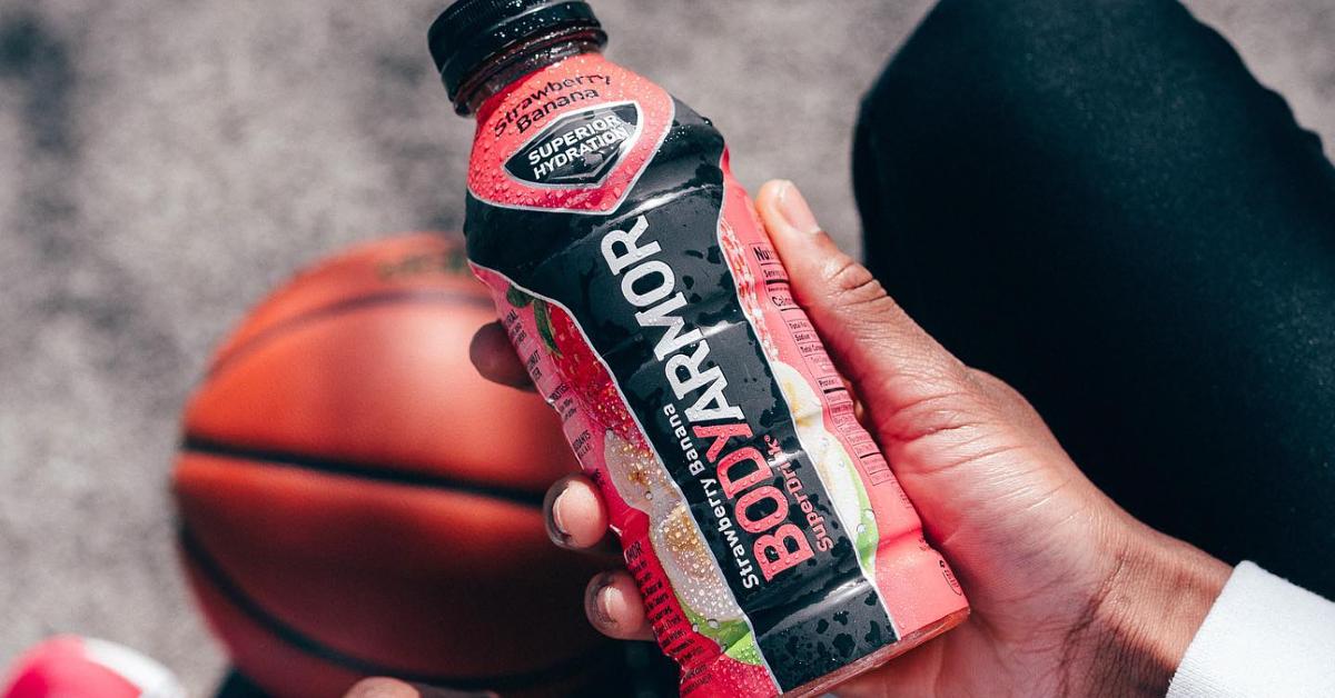 Photo of a hand holding a Bodyarmor sports drink with a basketball in the background