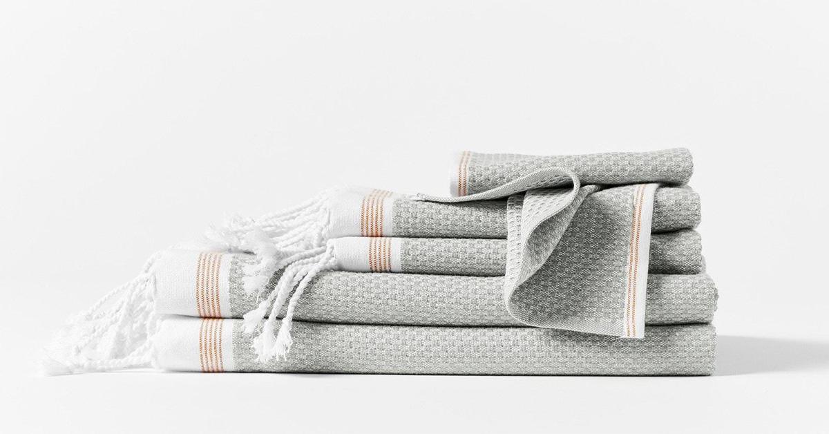 Stack of Turkish towels in grey, white, and orange with fringe