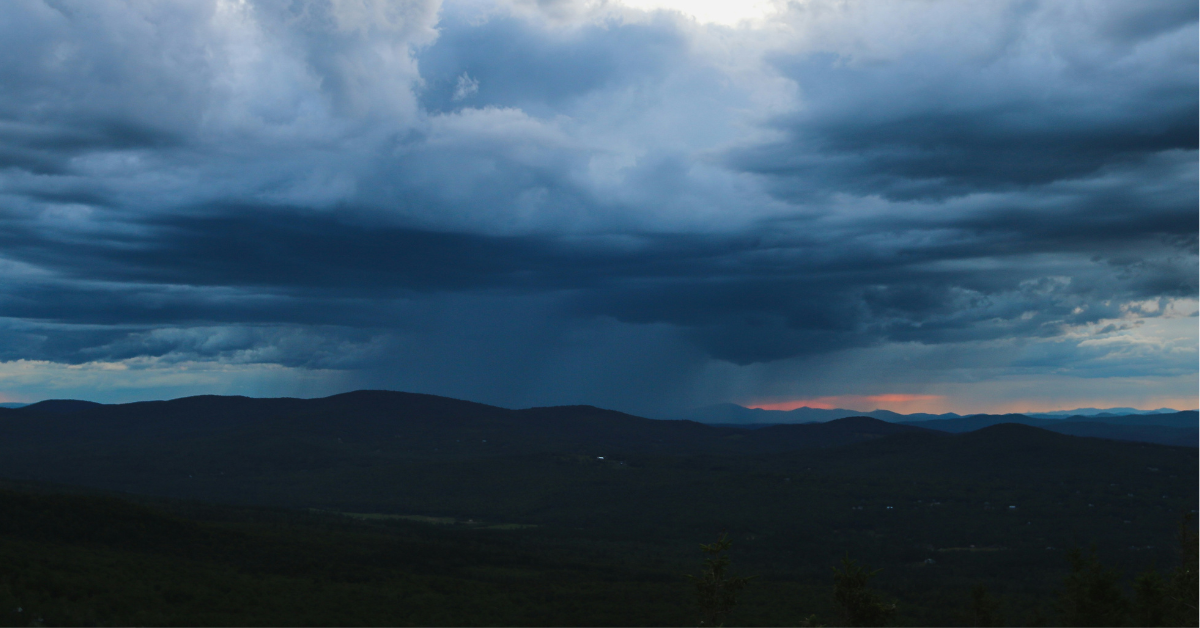 A massive storm system forms in the distance over a mountain range