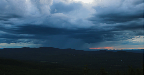 A massive storm system forms in the distance over a mountain range