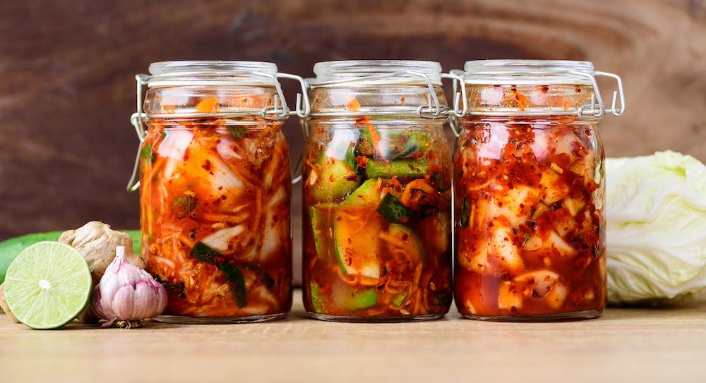 Three jars of kimchi on a wooden table.