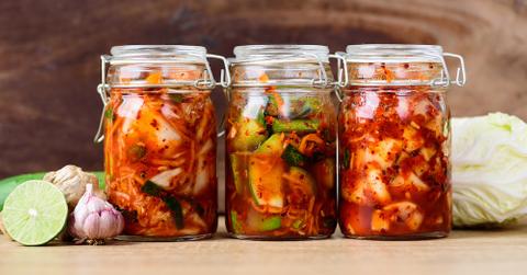Three jars of kimchi on a wooden table.
