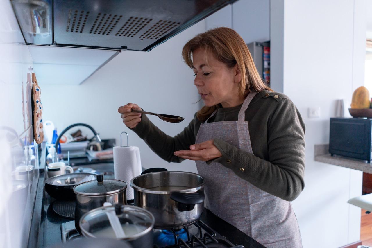 Person standing next to stove and blowing on hot food before tasting it