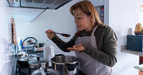 Person standing next to stove and blowing on hot food before tasting it