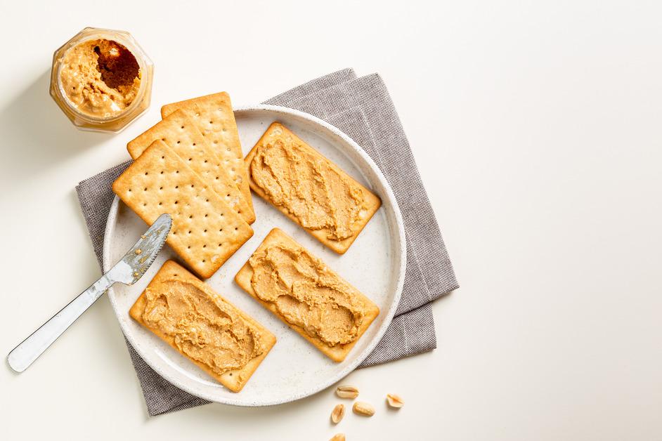 An overhead view of a plate of crackers with a knife and peanut butter.