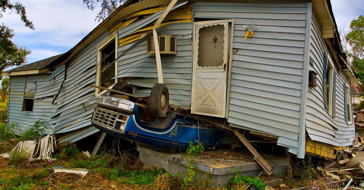 A blue car sticks out from under the foundation of a house