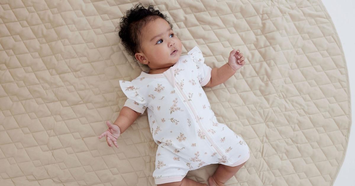 Baby in floral onesie lays on beige blanket