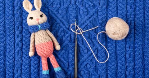 A completed pink and blue crochet bunny next to the hook and yarn that was used to create it.