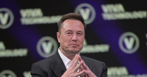 Elon Musk wears a suit, looking thoughtful and amused at a conference