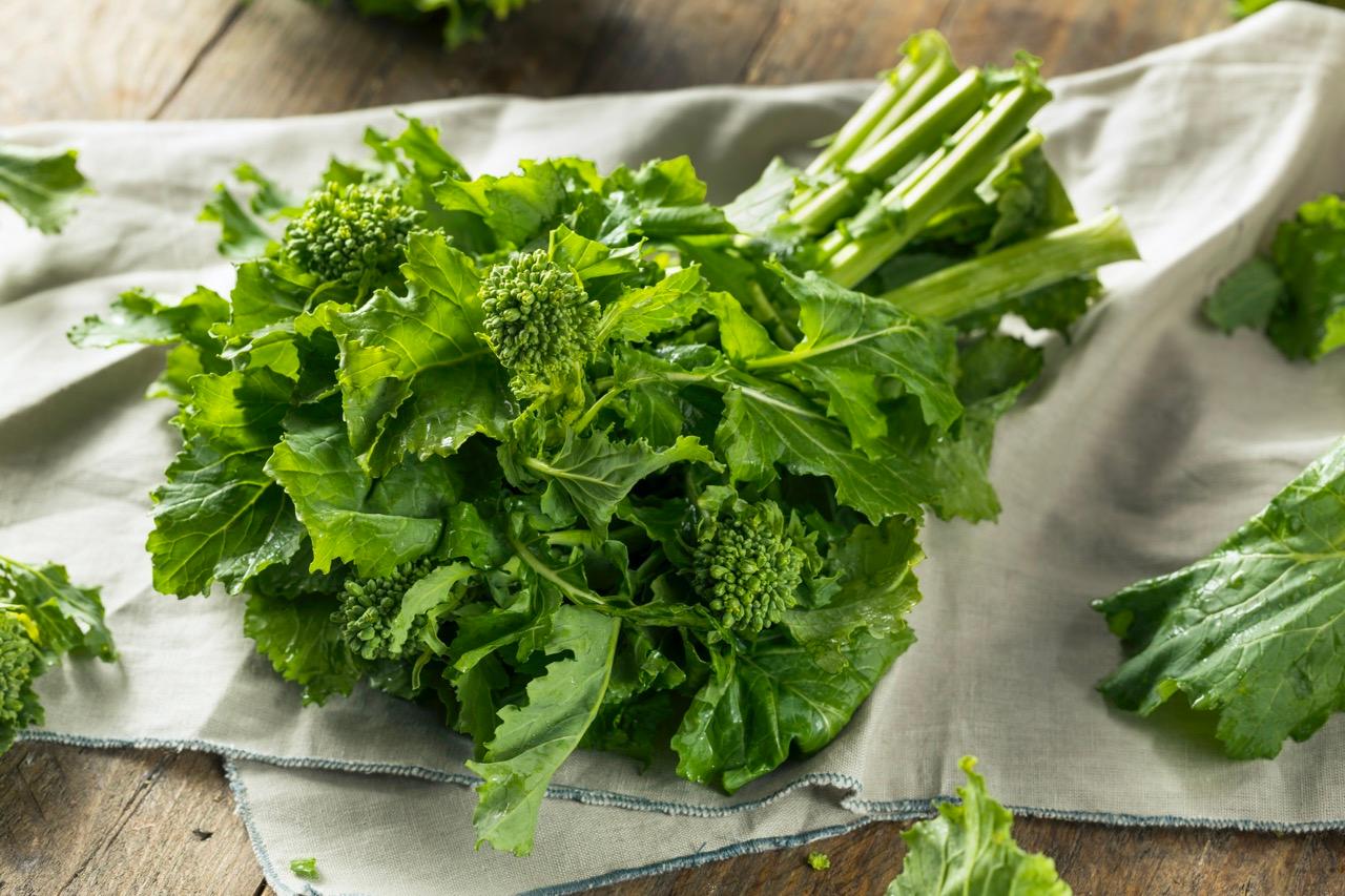 A bunch of uncooked broccoli rabe on a white cloth on a table.