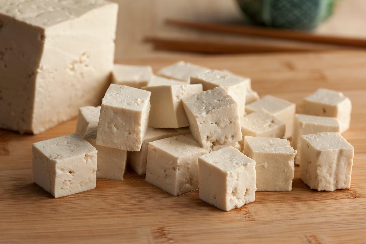 A block of tofu is cut into smaller chunks on a cutting board.