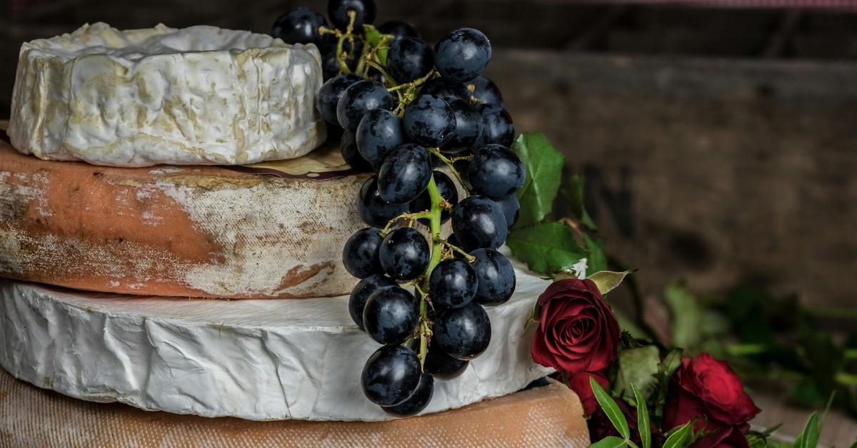 Brie cheese sits in a stack alongside some grapes and roses