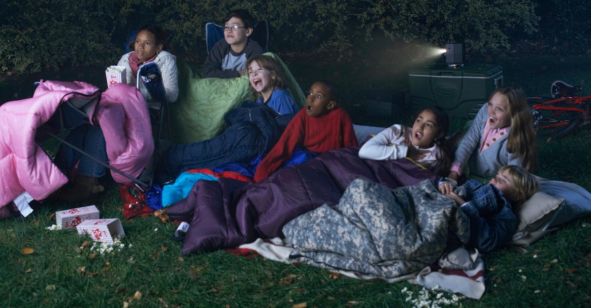 Group of schoolchildren watching an outdoor movie at a sleepover. 