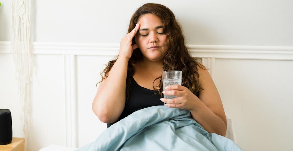 A woman is in bed sick with a glass of water.