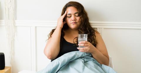 A woman is in bed sick with a glass of water.