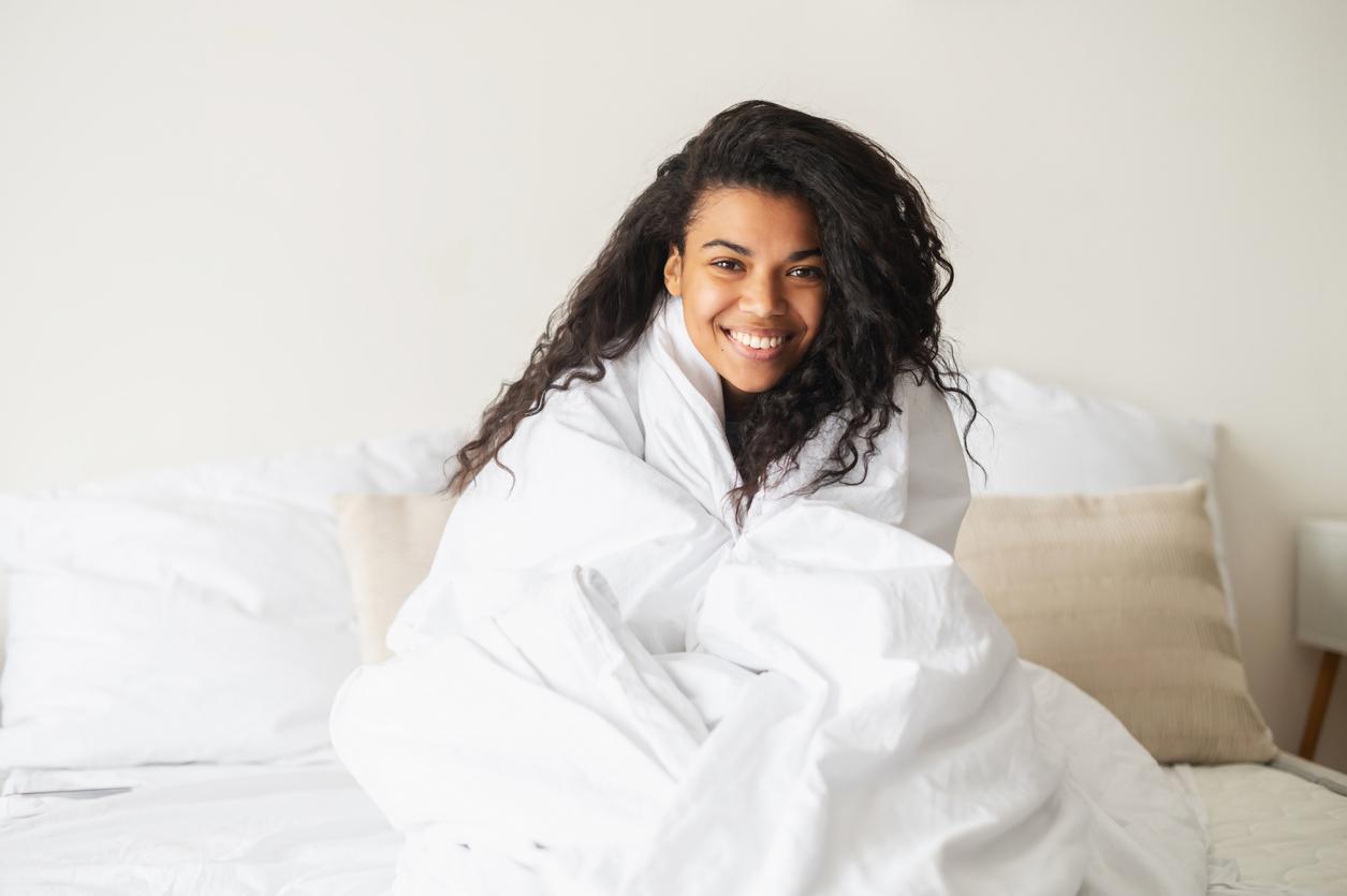 A smiling woman is wrapped in a white blanket in bed.