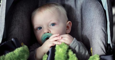 A small baby sits in a car seat with a stuffed animal