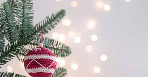 A close up view of a red and white crocheted ornament hanging from a Christmas tree.