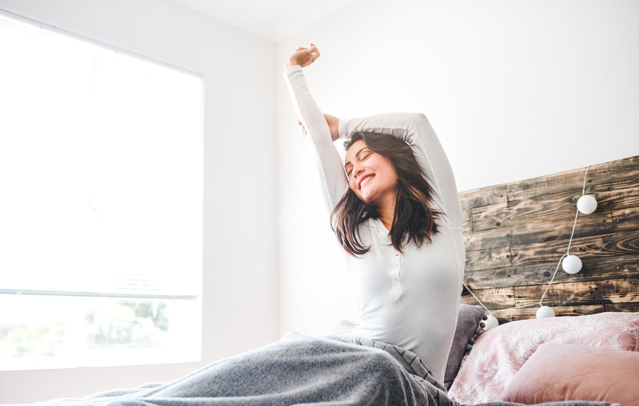 A woman stretches in bed while smiling at the beginning of the day.