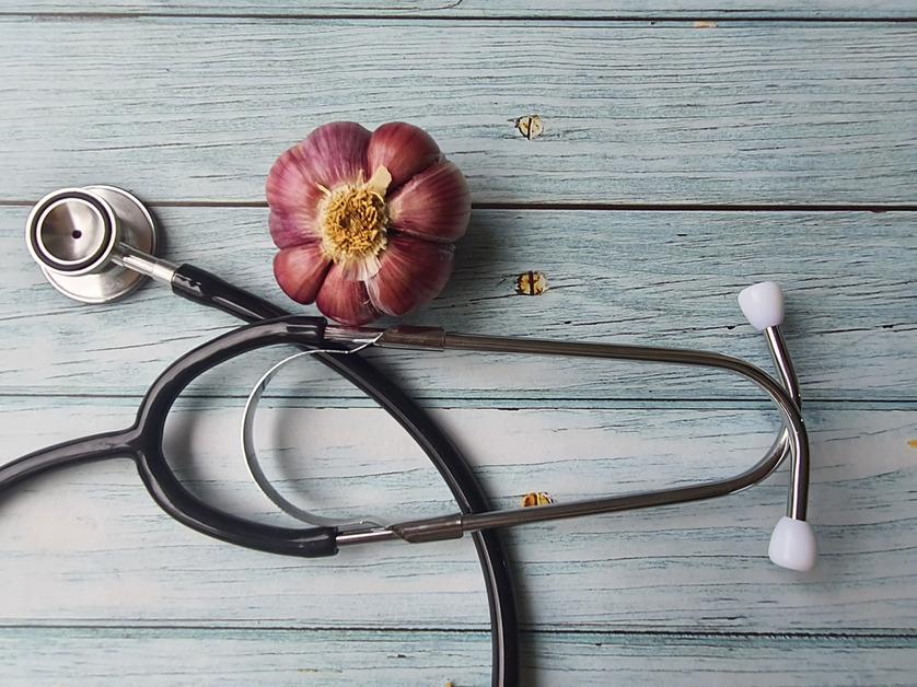 An overhead photo of a stethoscope on a wooden surface next to a purple garlic bulb. 