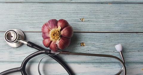 An overhead photo of a stethoscope on a wooden surface next to a purple garlic bulb.