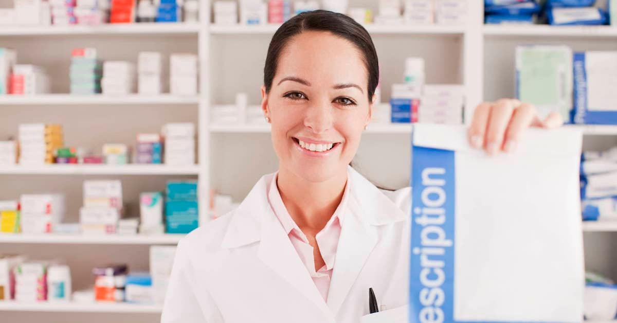 Smiling pharmacist in a drug store holding up a package of prescription drugs