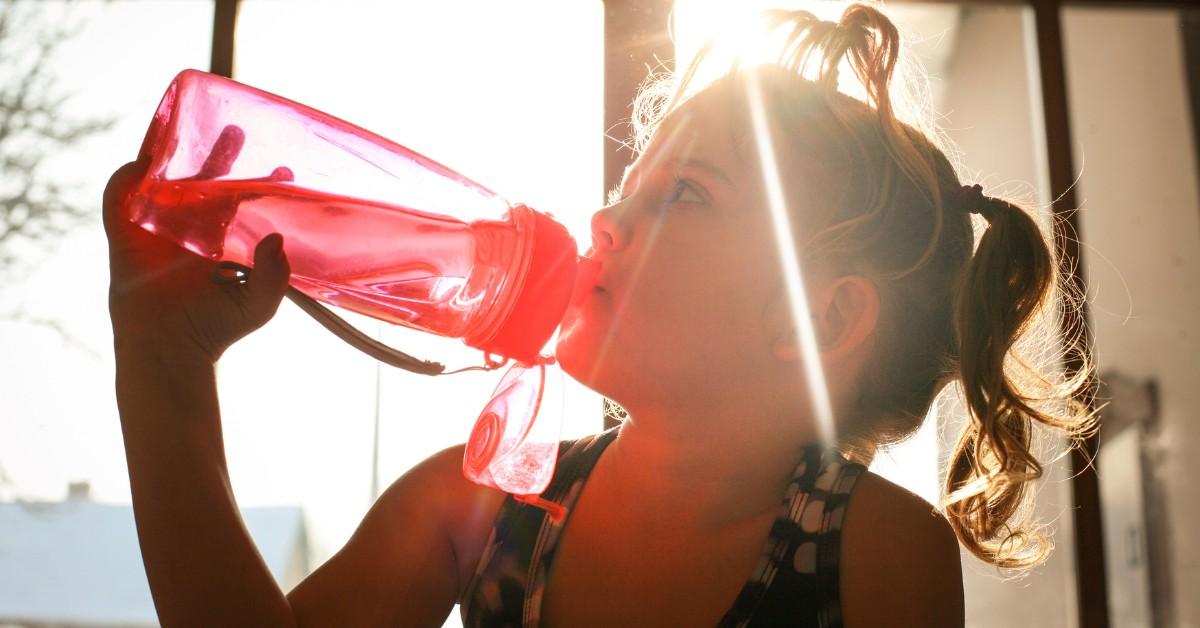 Little girl drinking water out of a pink bottle