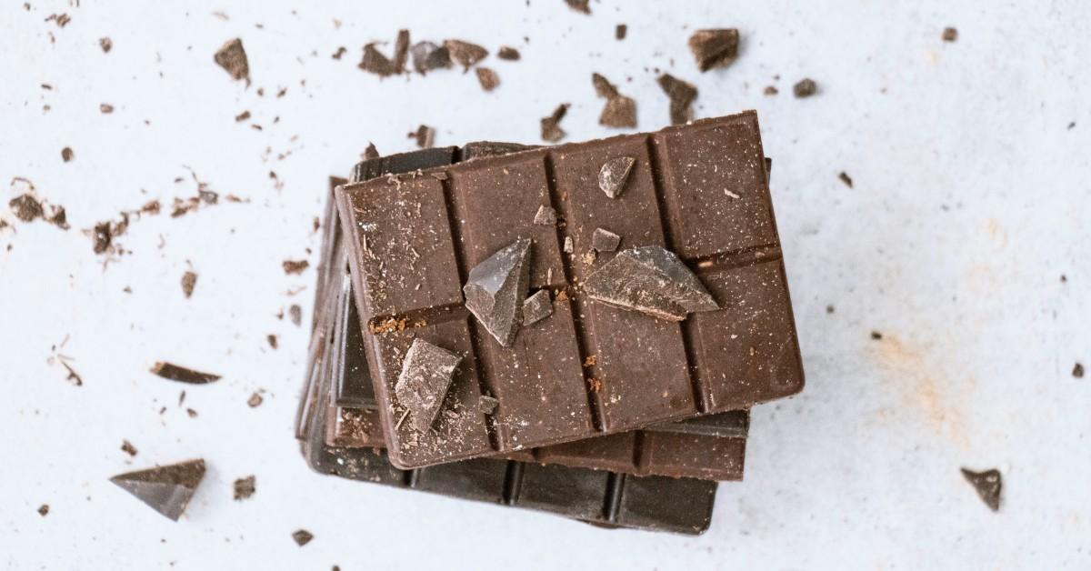 A broken chocolate bar sits on a white surface amongst bits of chocolate chunks