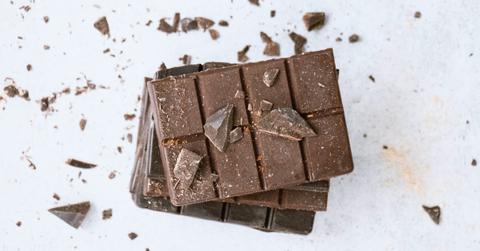 A broken chocolate bar sits on a white surface amongst bits of chocolate chunks
