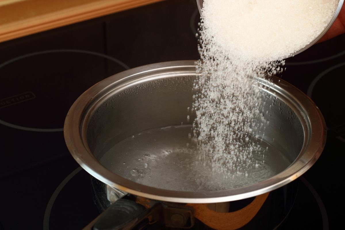 White sugar being poured into a silver pot on the stove