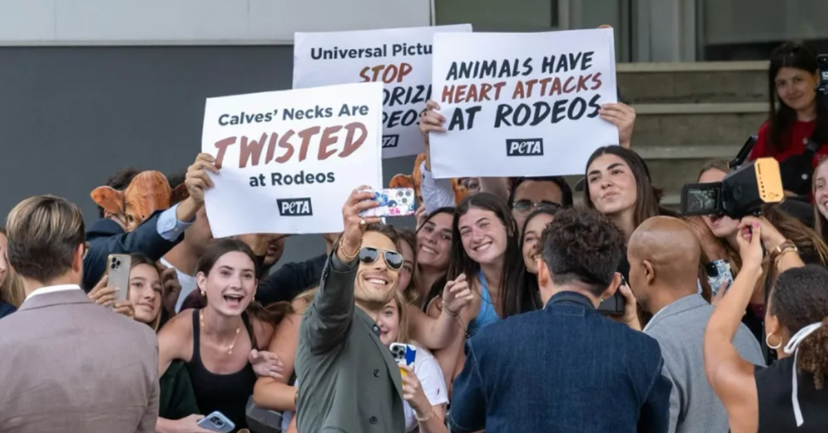 Glen Powell poses with fans in front of PETA protesters outside of the 'Twisters' premiere.