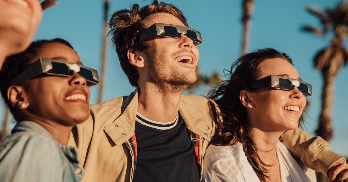 Group of young people wearing solar eclipse glasses at the beach. 