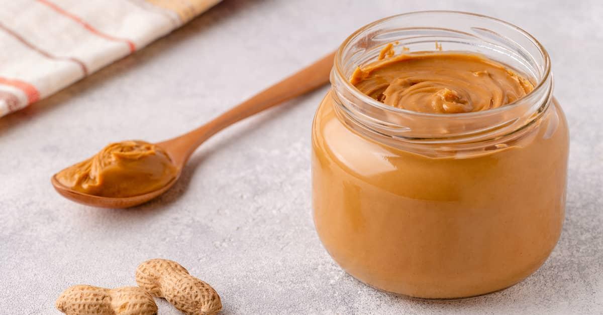 Jar of smooth peanut butter with a spoon full of PB next to it and some peanus in shells to the side