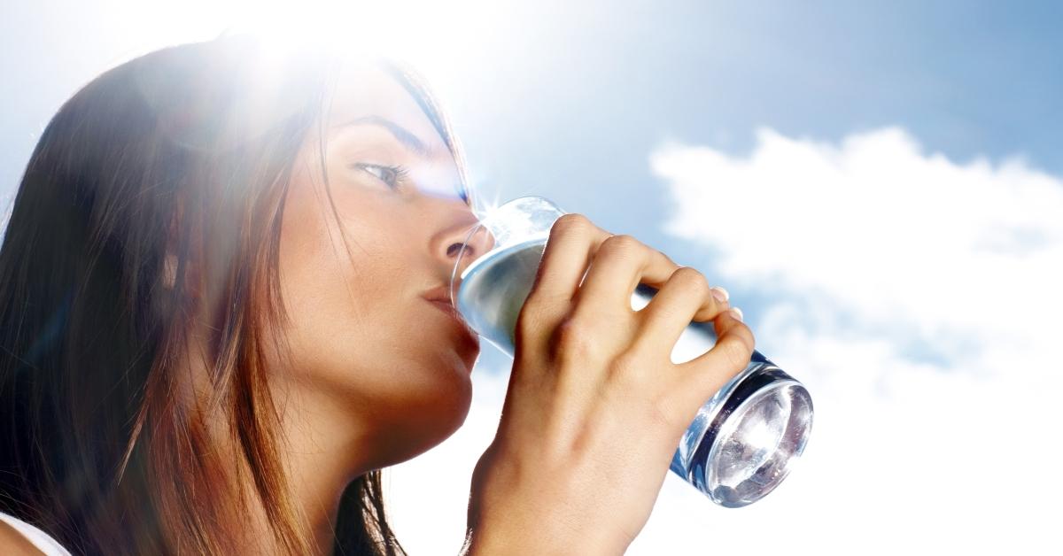 Woman drinking a glass of water in front of a blue sky background.