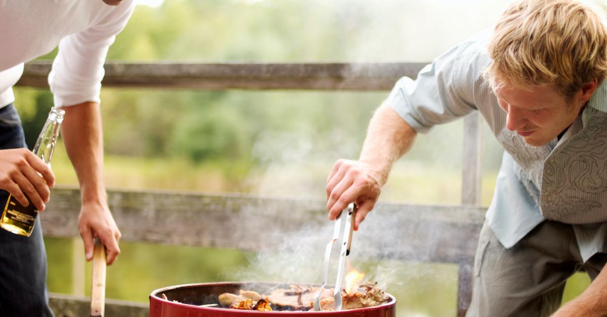 Two men barbecuing on an open grill, holding beers. 