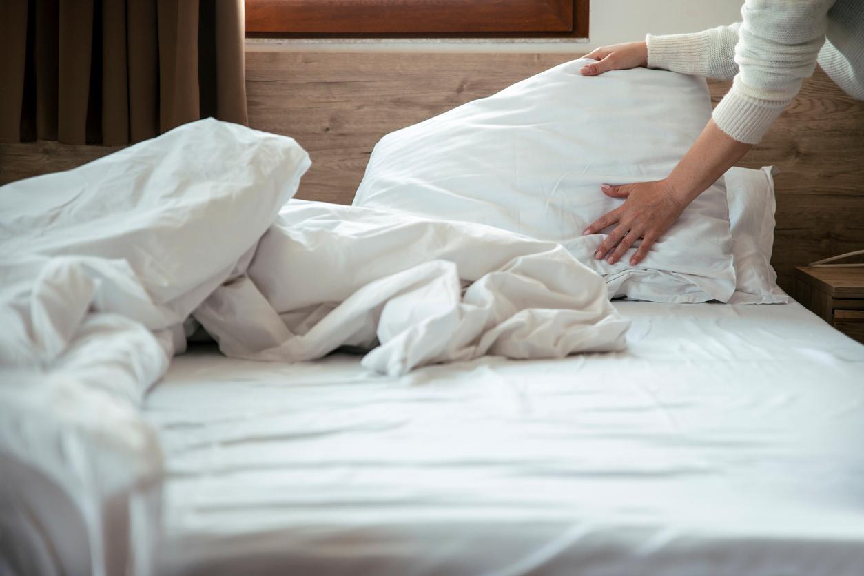 Close up view of a person adjusting white pillows and sheets on a bed.