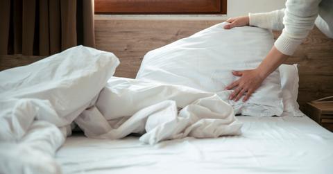 Close up view of a person adjusting white pillows and sheets on a bed.