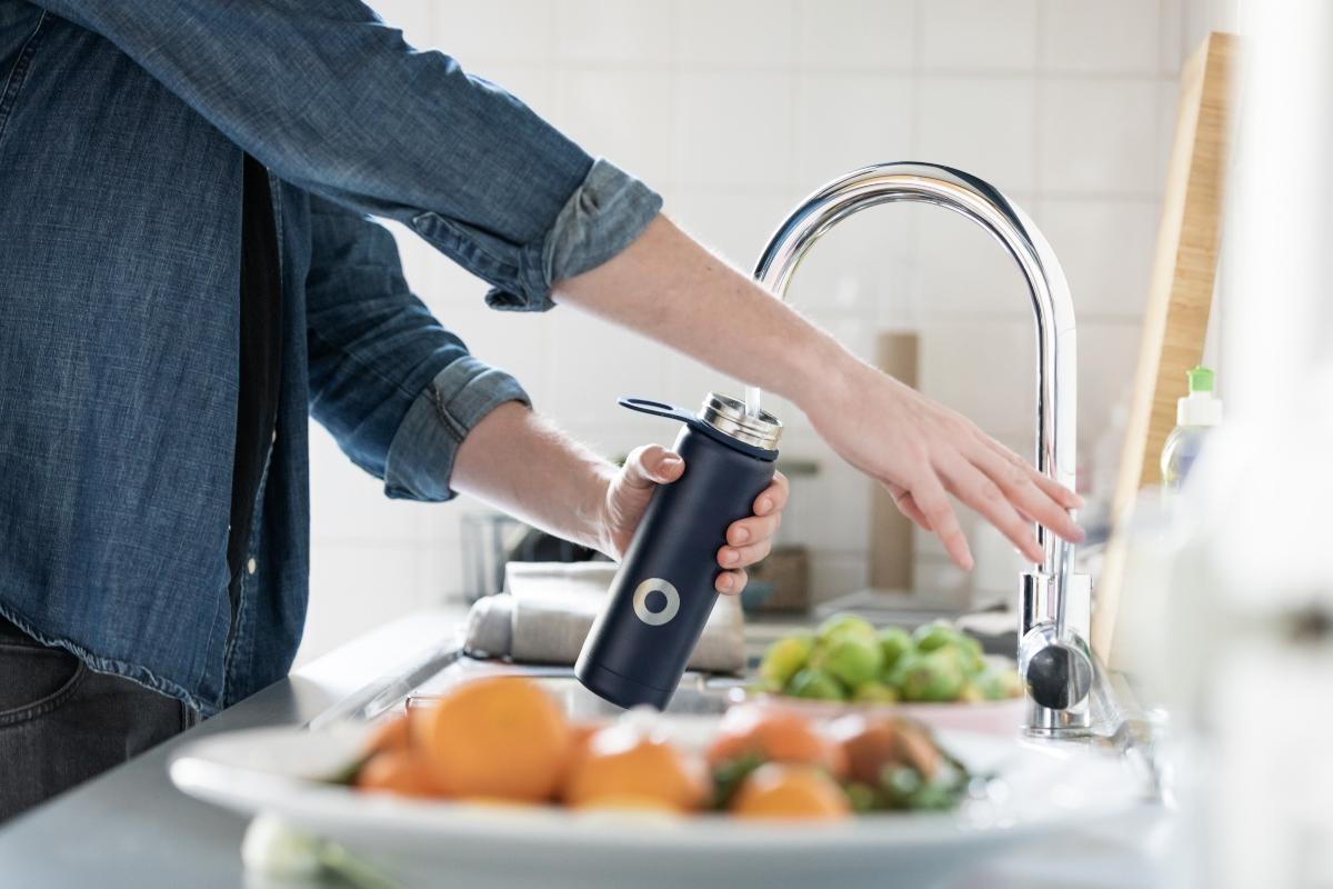 man in denim shirt filling water bottle at faucet