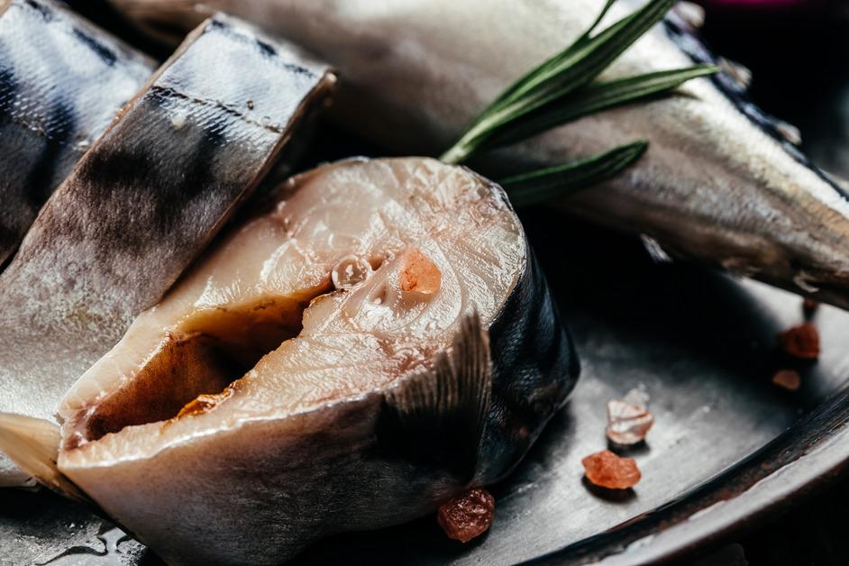 A piece of fish cut open resting next to other pieces of fish and salt bits. 