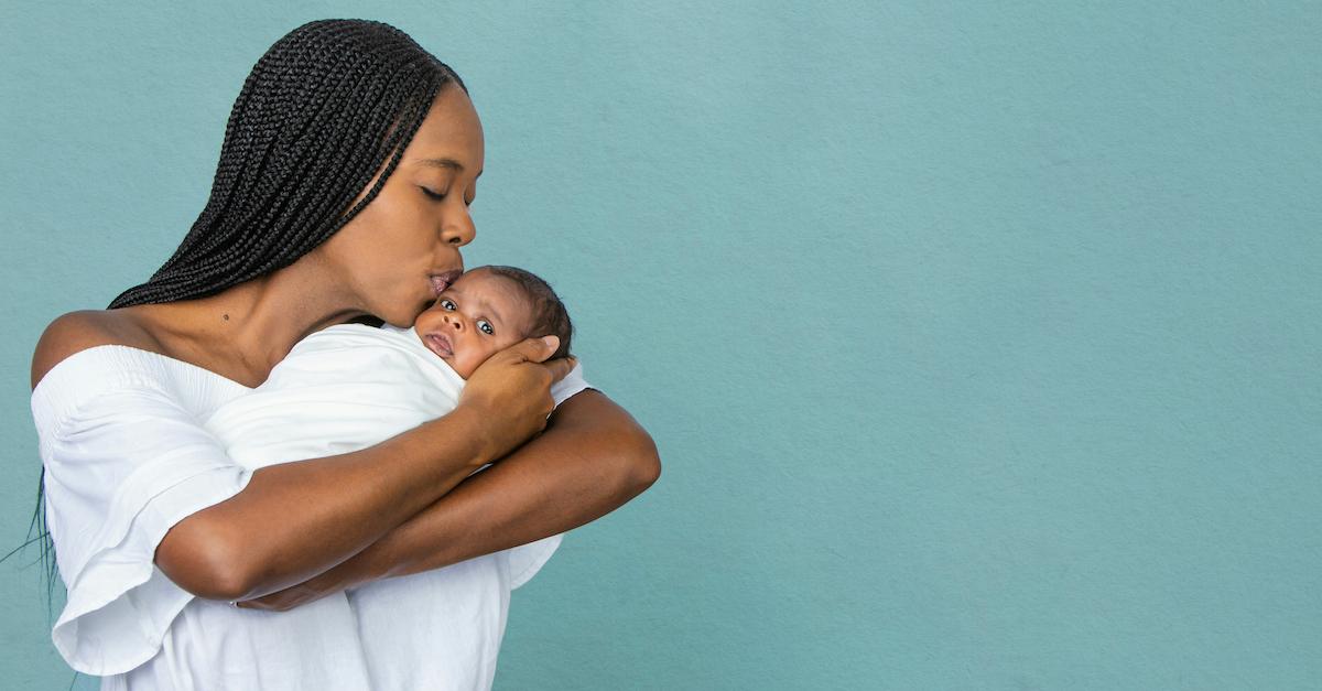 A Black woman kisses her baby in front of a blue wall