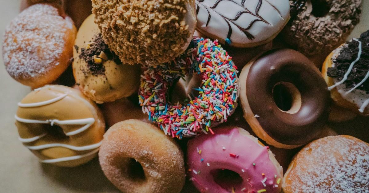 An assortment of doughnuts that include chocolate, sprinkles, and powdered, are piled up on a table