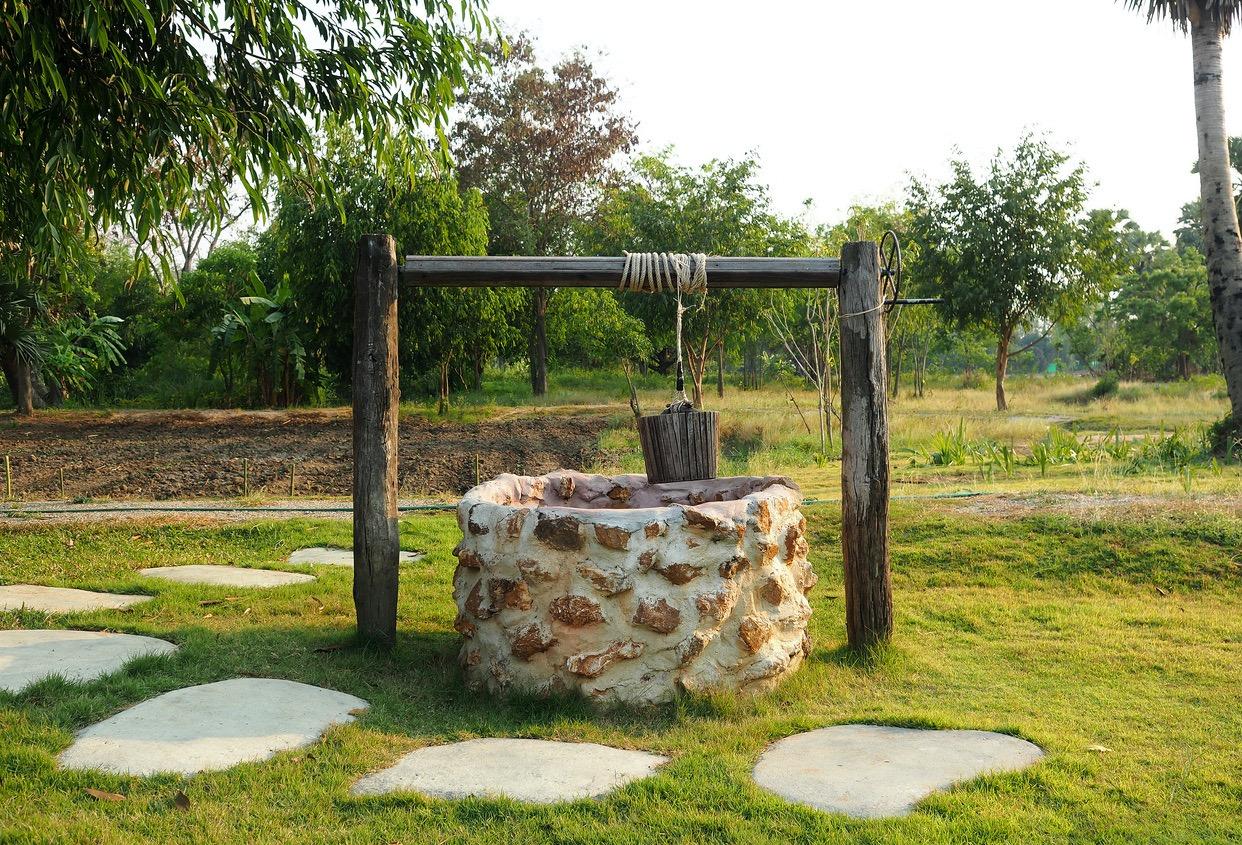 An old-school brick well in a field of green grass and trees.