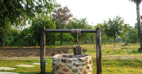 An old-school brick well in a field of green grass and trees.