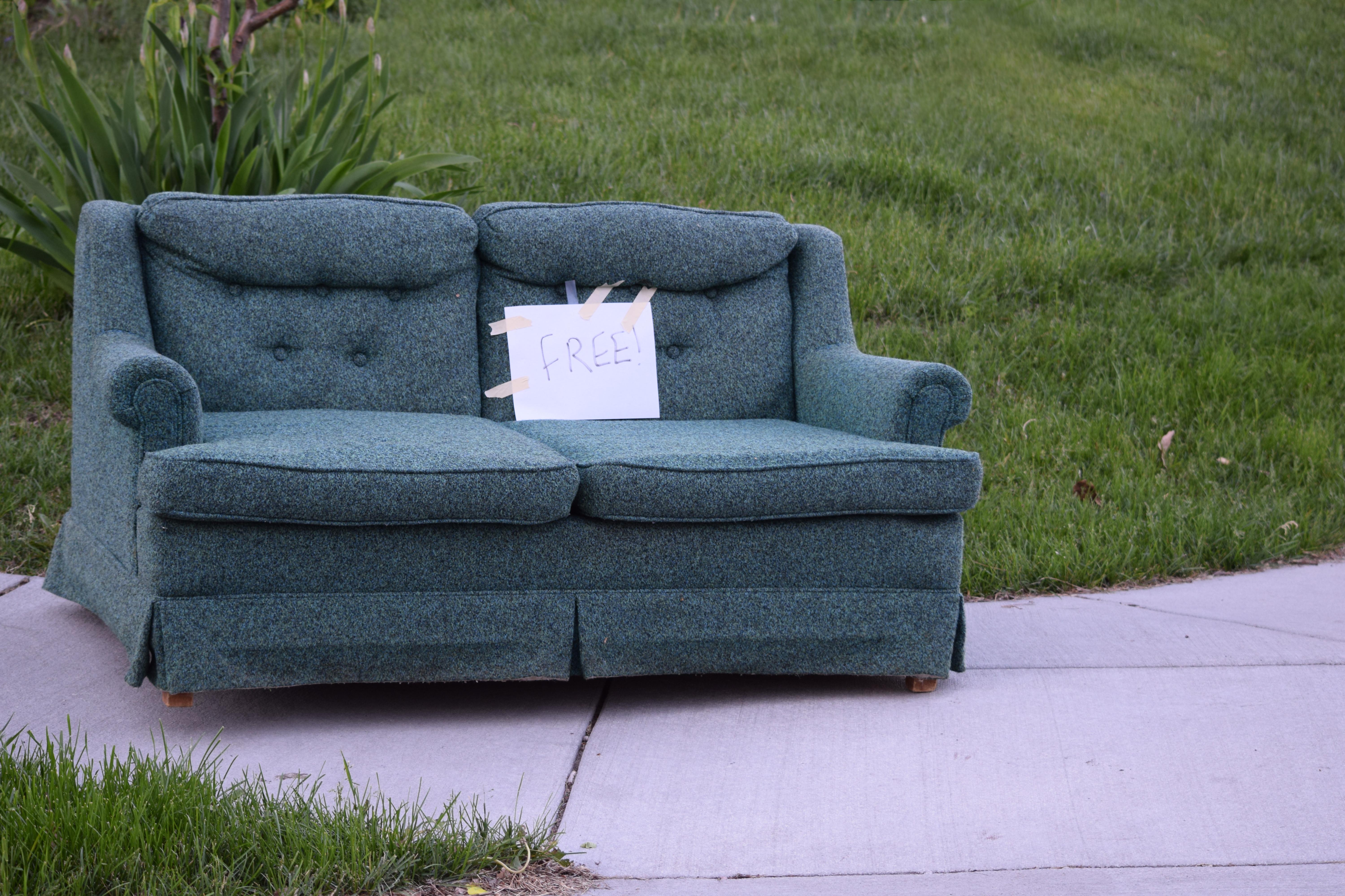 A blue couch with a "free sign" on a sidewalk