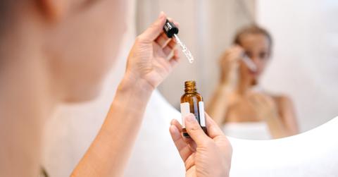 Photo of woman holding a skincare bottle and dropper in front of a mirror