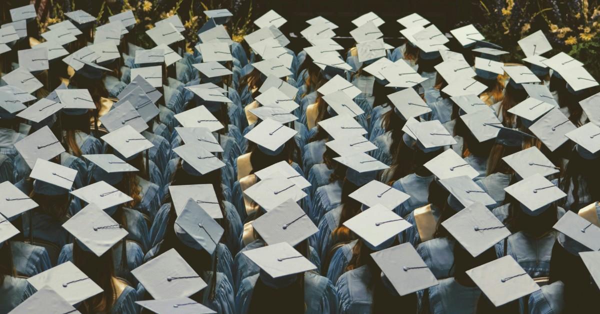 Graduates stand shoulder to shoulder while wearing their cap and gowns