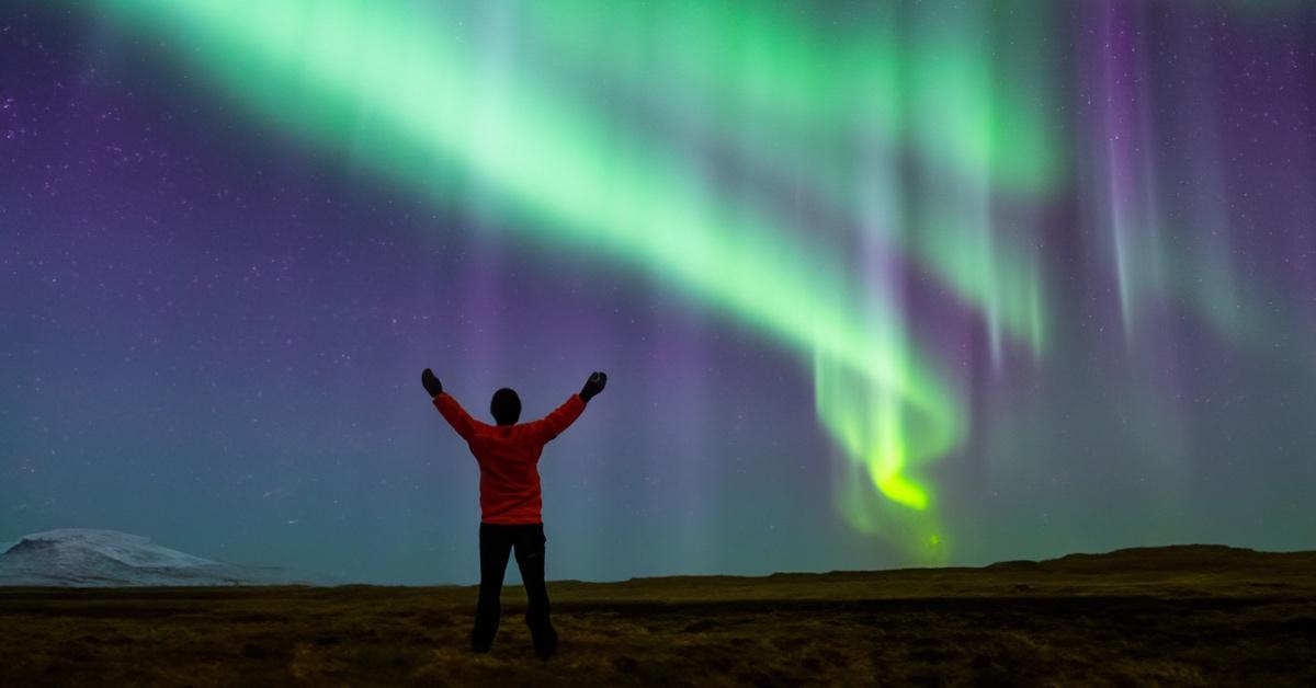 Man in Iceland standing on the grass in front of the Northern Lights.